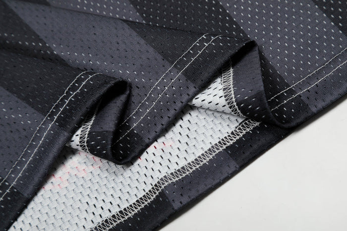 Close-up of black football jersey fabric with white mesh lining and stitched seams, featuring a perforated sport chain graphic pattern