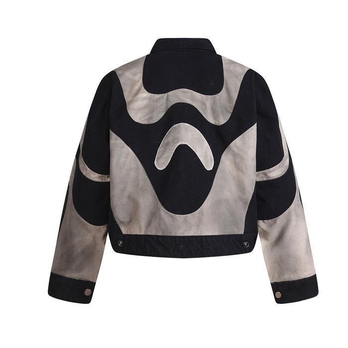 Back view of the cropped black and grey jacket showing curved abstract patchwork panels and snap cuffs