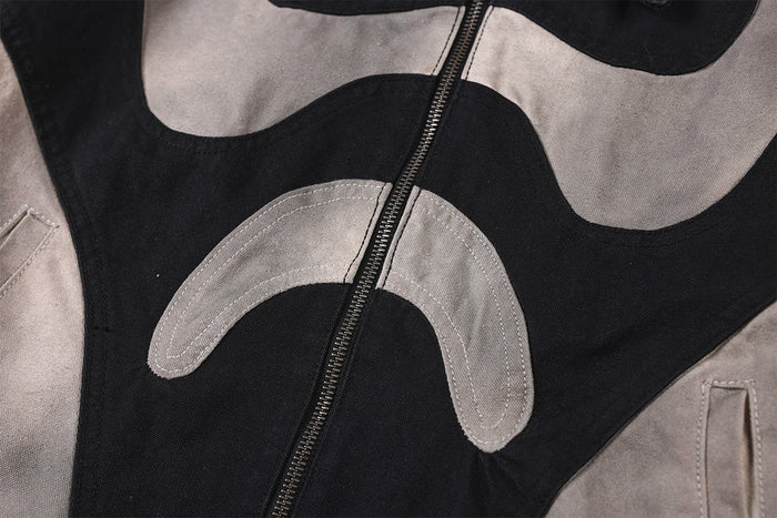Close-up of the jacket front showing a silver-grey curved patch, black panels, and central metal zipper