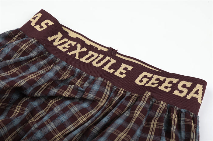 Close-up of burgundy knit elastic waistband with beige lettering above plaid fabric