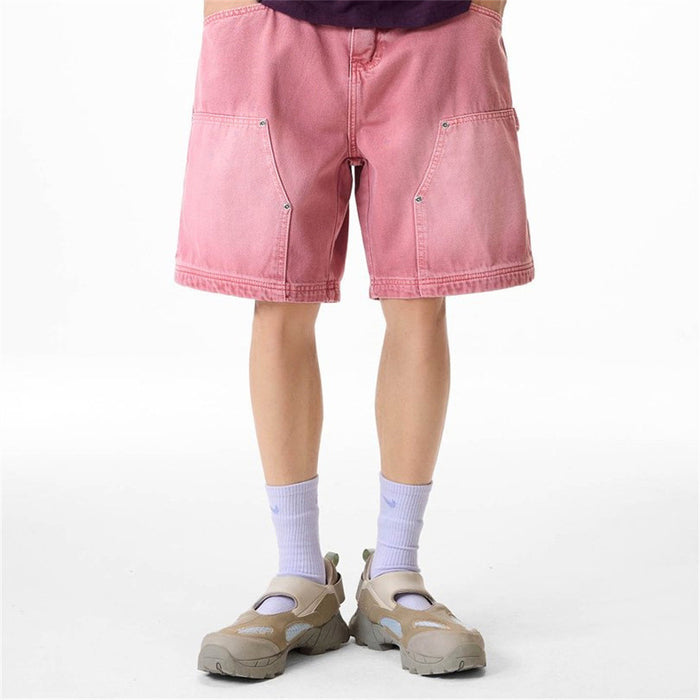 Pink carpenter-style denim shorts worn from the front with angled utility pockets and wide legs