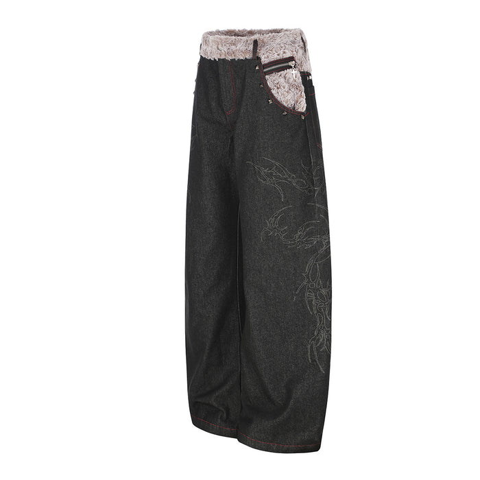 Angled front view of black baggy jeans showing the wide leg, beige plush waistband, zipper pocket, and side graphic