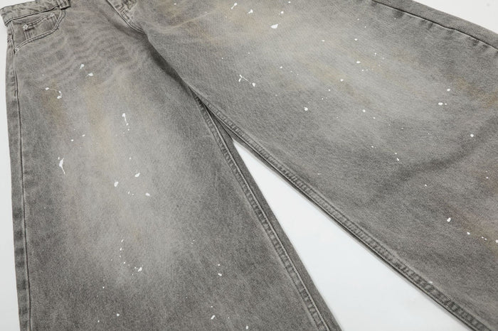Close-up of grey denim legs showing acid-washed shading, fine twill texture and scattered white paint splatters