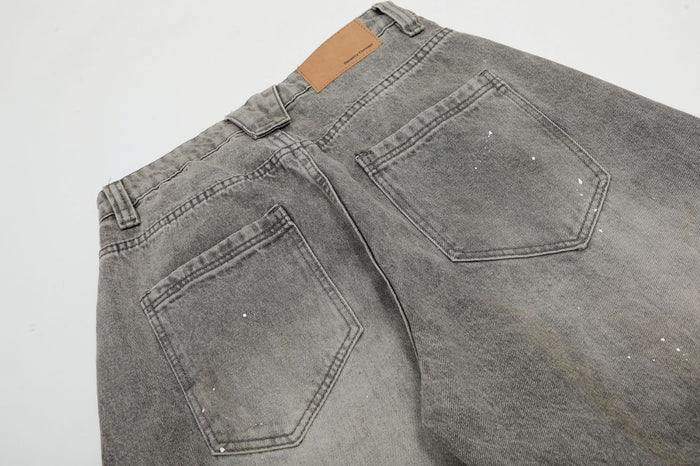 Close-up of the jeans back showing two angular stitched pockets, waistband and grey acid-washed denim