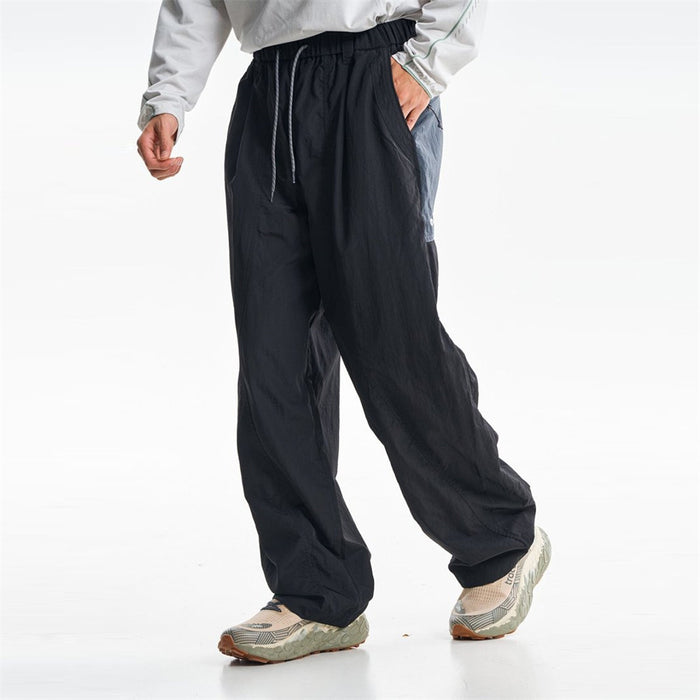 Black baggy parachute pants shown in a front three-quarter view with drawstring waist and side pockets