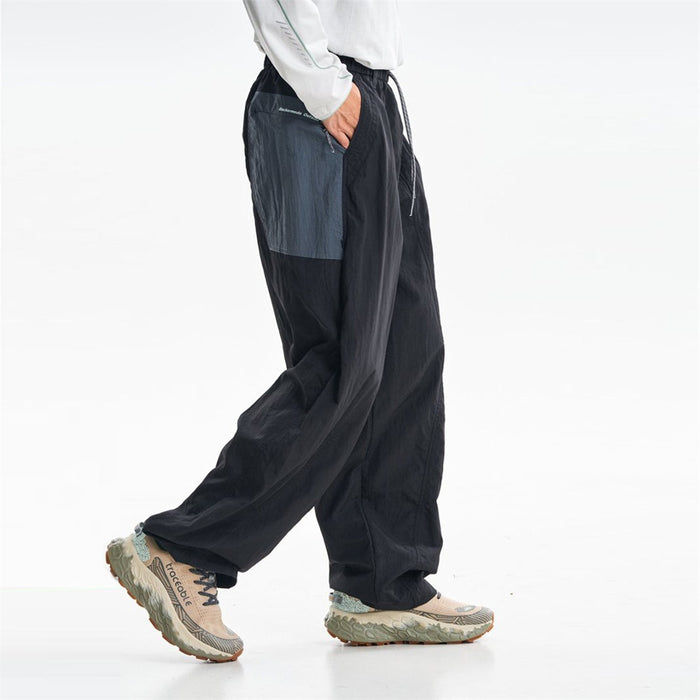 Black parachute pants shown from the side with a contrasting gray side pocket panel