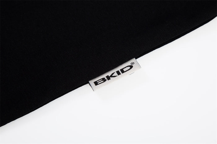 Close-up of black Bkid raglan T-shirt hem with visible branded label on a clean white background