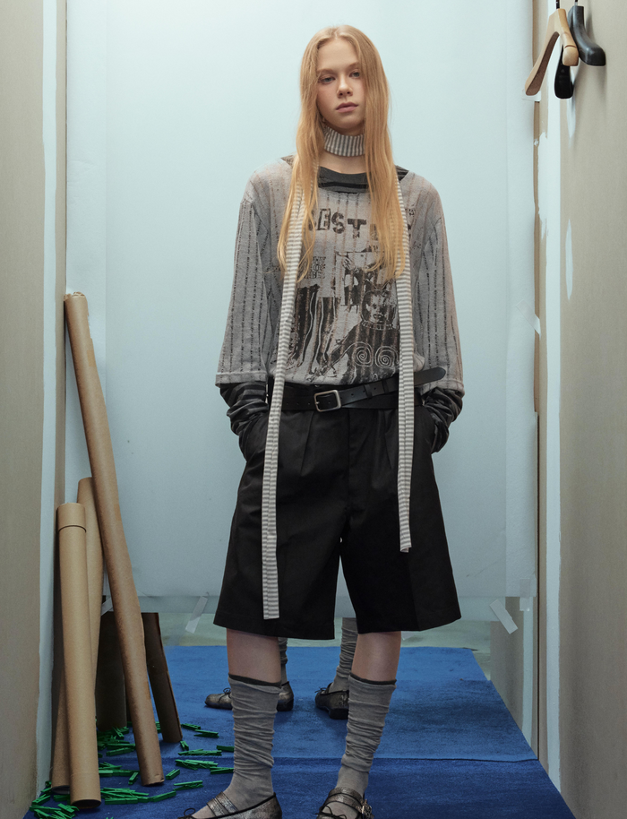 Model wearing gray distressed graphic sweater with striped sleeves and black shorts