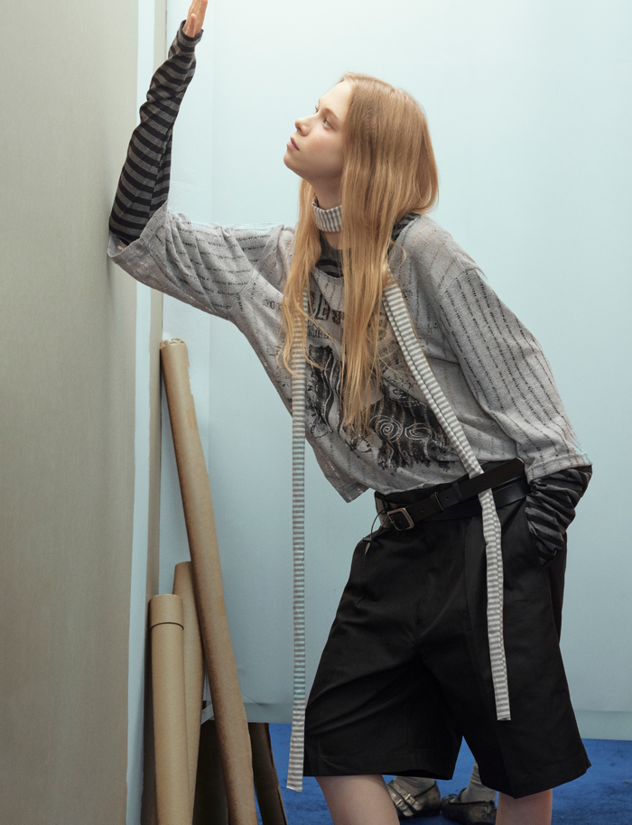 Side view of gray layered sweater top with black striped sleeves on model
