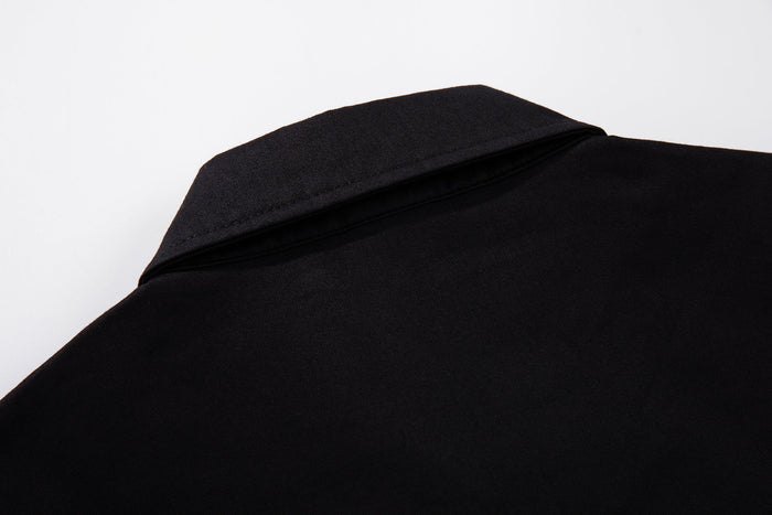 Close-up of a black button-up shirt collar and shoulder with smooth fabric and subtle streetwear styling