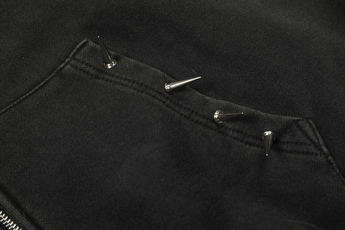 Close-up of silver metal spikes attached along the edge of a black hoodie pocket
