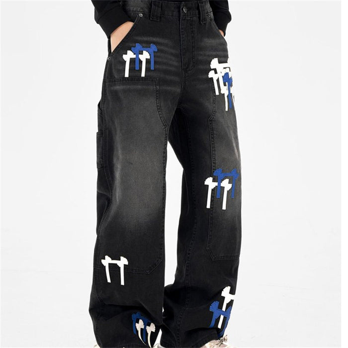 Angled front view of black cargo jeans showing wide legs, side pockets, and white and blue cross patches