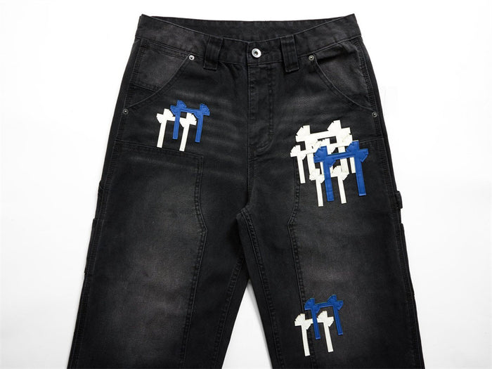Upper front detail of black cargo jeans showing belt loops, front pockets, and white and blue cross patches