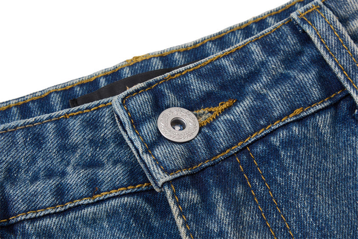 Detailed view of the metal waistband button and reinforced golden stitching on blue denim
