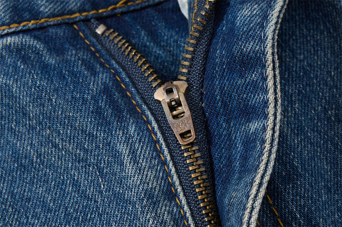 Close-up of the partially opened zipper fly with metal teeth and golden stitching on blue denim
