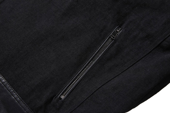 Close-up of a vertical silver zippered pocket set into the black denim front panel