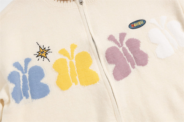 Cream cardigan chest close-up showing blue, yellow, pink, and white butterfly motifs with an oval patch