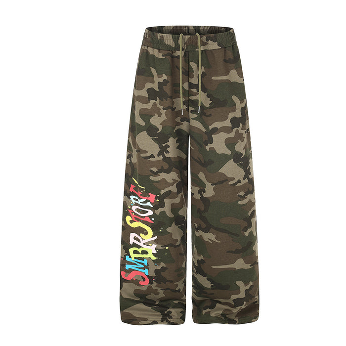Wide-leg camouflage sweatpants with multicolor graffiti letter print on left leg and paint splatter detail, front and back vi