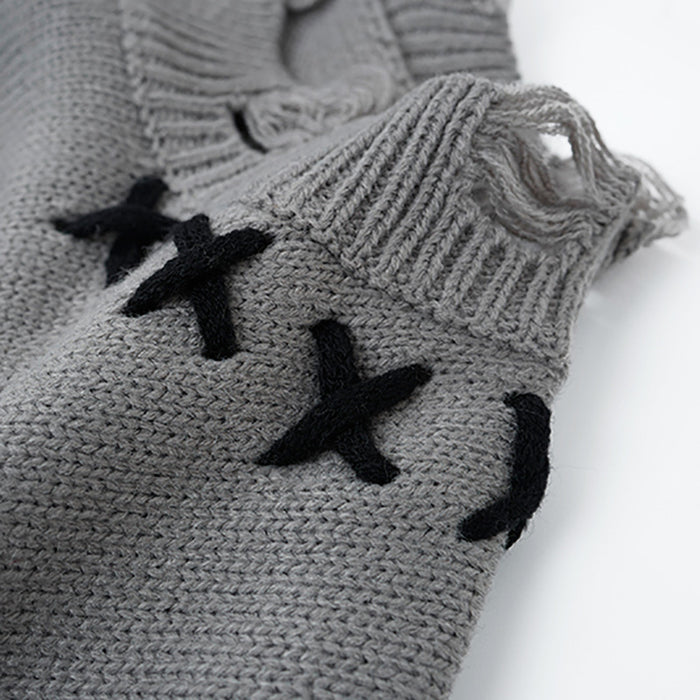 Close-up of distressed gray knit shoulder showing ribbed edging, loose yarn loops, and black X stitching