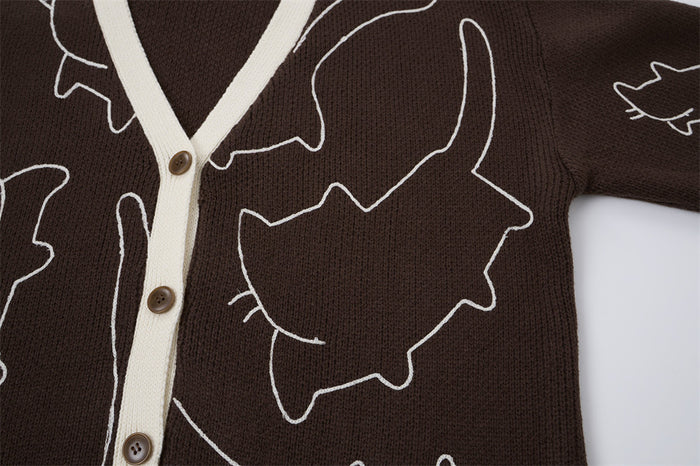 Close-up of a white cat outline on the brown knit cardigan beside the cream button placket