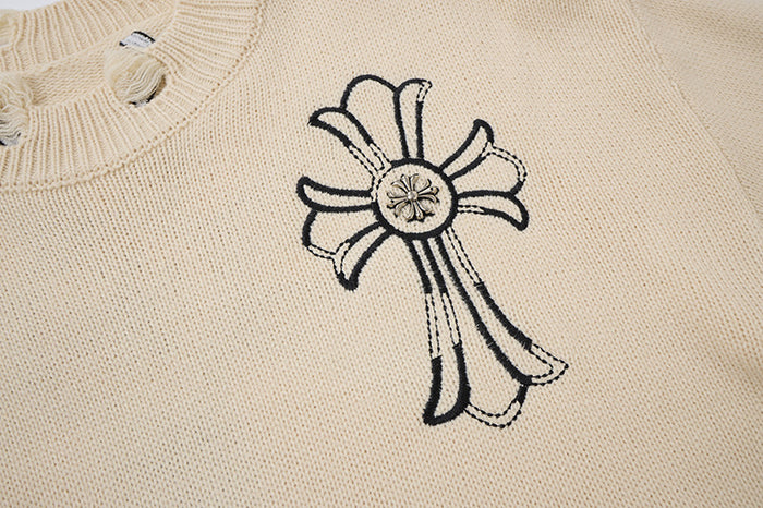 Close-up of black outlined cross embroidery on cream knit fabric, showing detailed stitched design