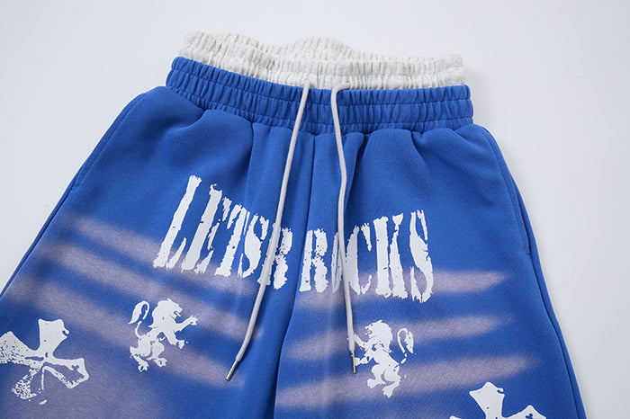 Close-up of blue sweatpants showing gray faux waistband, white drawcord, distressed lettering, and faded stripe graphics