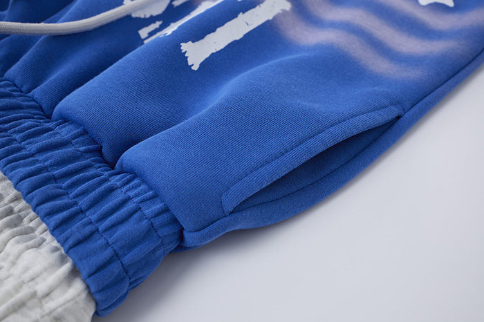 Close-up of blue sweatpants leg showing smooth knit fabric, side seam, gathered hem, and white drawcord