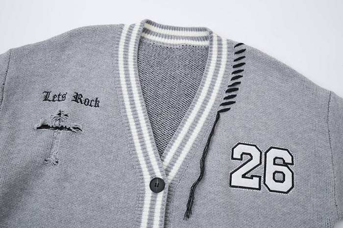 Close-up of gray cardigan front showing striped V-neck trim, button, number 26 patch, cross graphic and loose threads