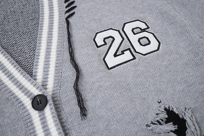 Close-up of gray knit cardigan showing the outlined number 26 patch, black button, striped trim and loose distressed threads