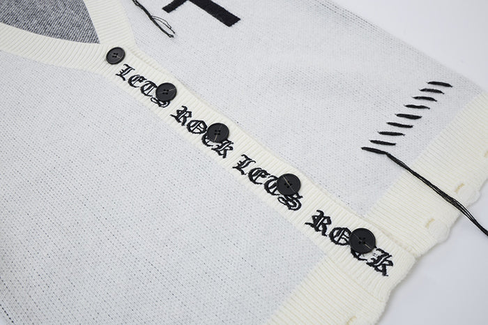 Close-up of a white cardigan showing black buttons, gothic lettering on the placket, cream ribbing, and loose threads