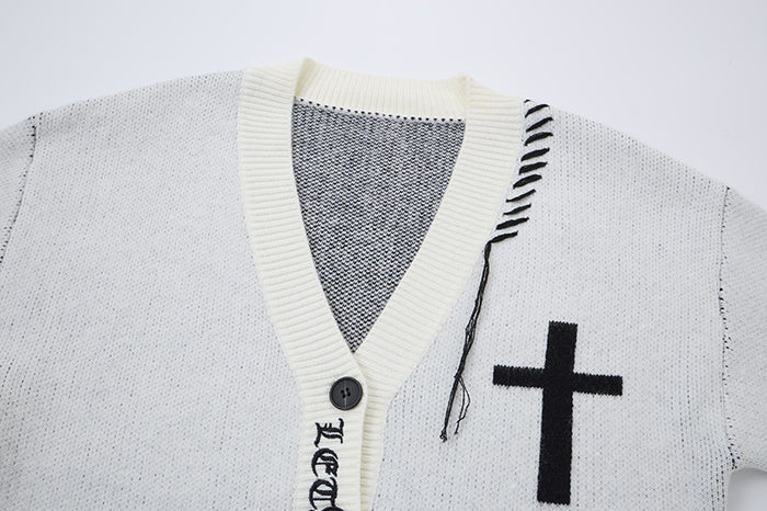 Close-up of the white cardigan V-neck showing cream ribbing, black cross motif, patterned stitching, and exposed threads