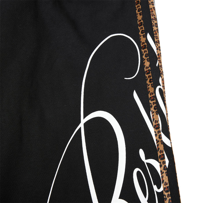 Close-up of white script print beside leopard side tape on black sweatpants
