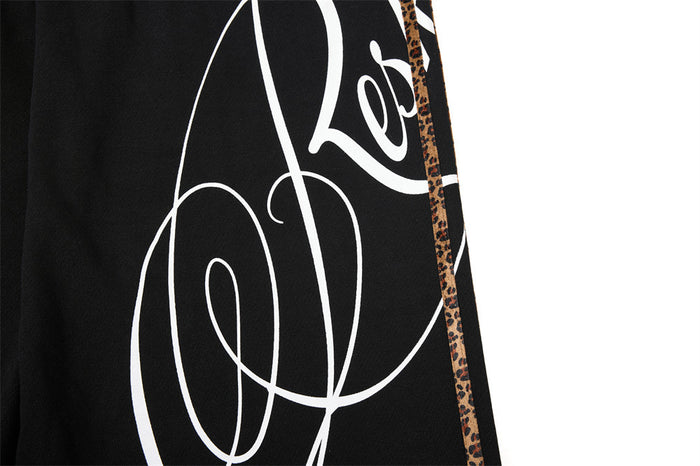 Close-up of large white script graphic and leopard side tape on black sweatpants