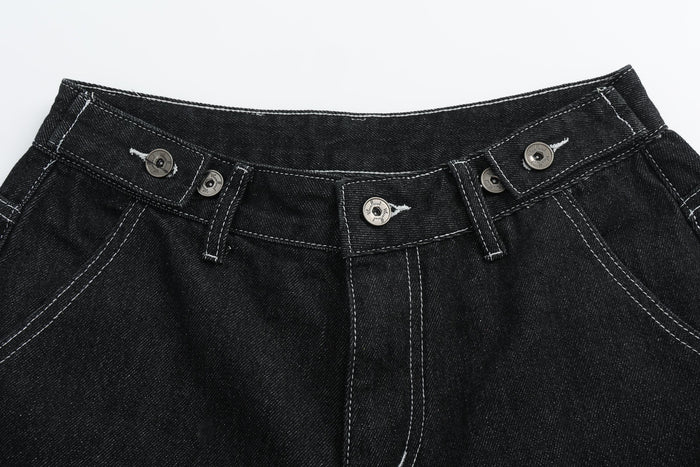 Close-up of black denim shorts waistband with silver button hardware and top stitching