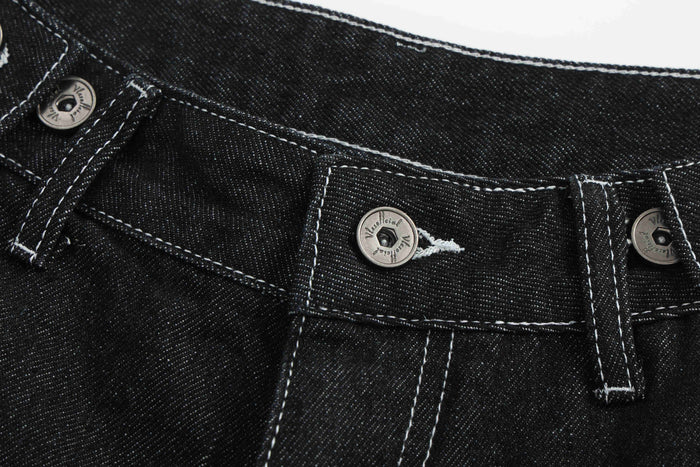 Waistband detail of black denim shorts with silver button fly and white stitching