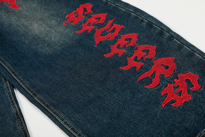 Close-up of red Gothic lettering embroidered vertically on a dark blue denim leg