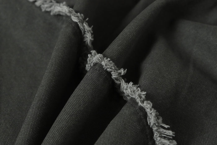 Close-up of gray woven jacket fabric showing a raised, frayed seam with loose fibers