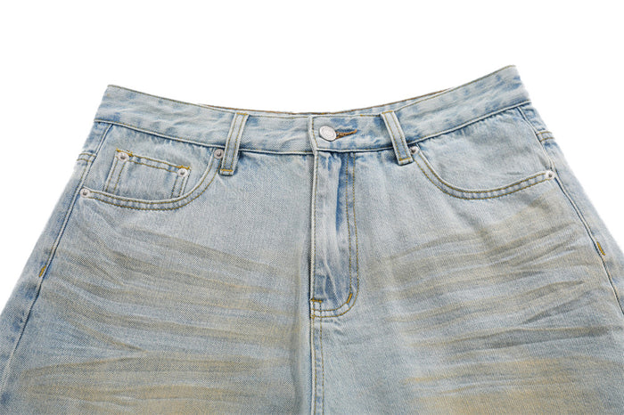Front waist detail of light blue distressed denim skirt shorts with button fly and faded whiskering