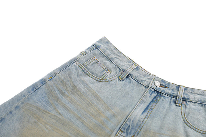 Angled close-up of distressed light blue denim waistband, front pocket, and button closure