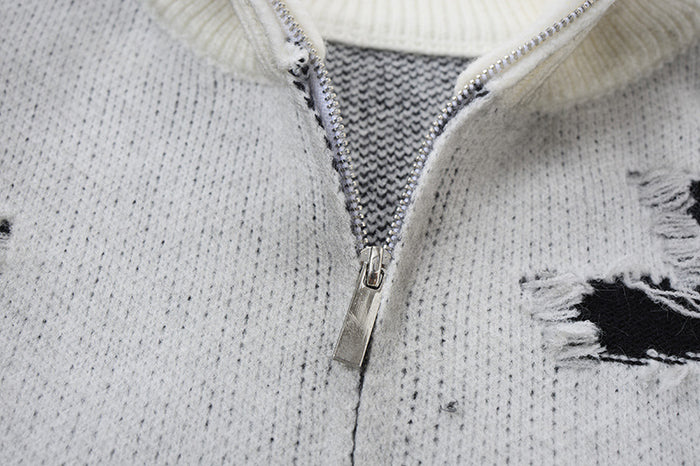 Close-up of the silver zipper, knit texture, and frayed black distressed opening on a light gray cardigan