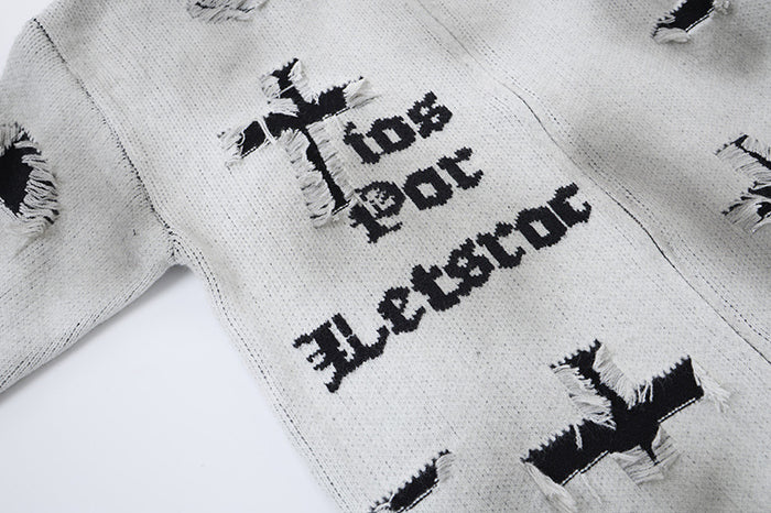 Close-up of a light gray cardigan front with black printed lettering, cross-like graphics, and distressed knit details