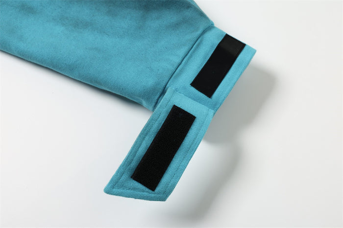 Teal sleeve hem with black rectangular patch details on the cuff tab