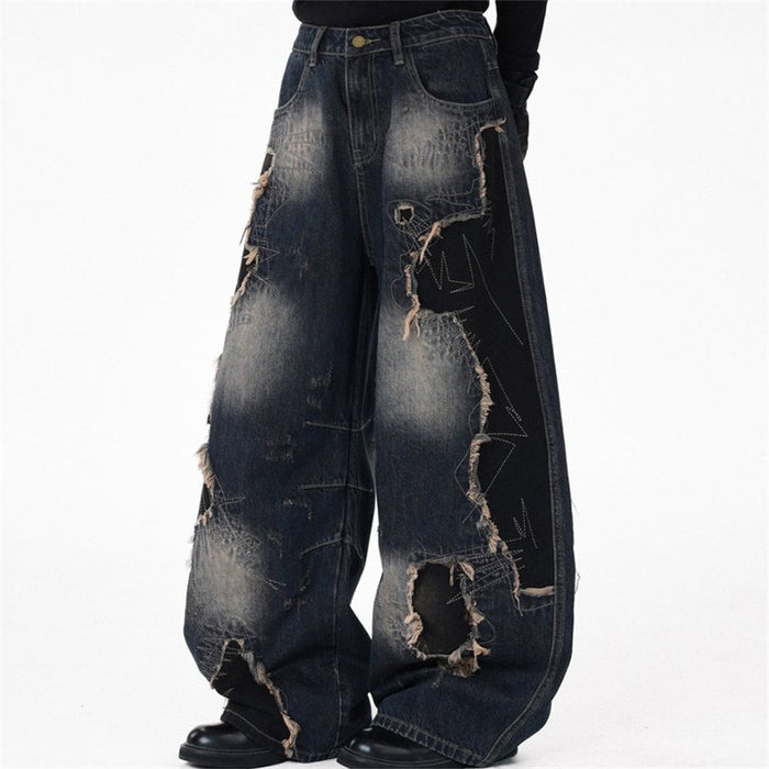 Model wearing dark blue baggy wide-leg jeans from the front, showing faded denim, black patch panels, and frayed rips