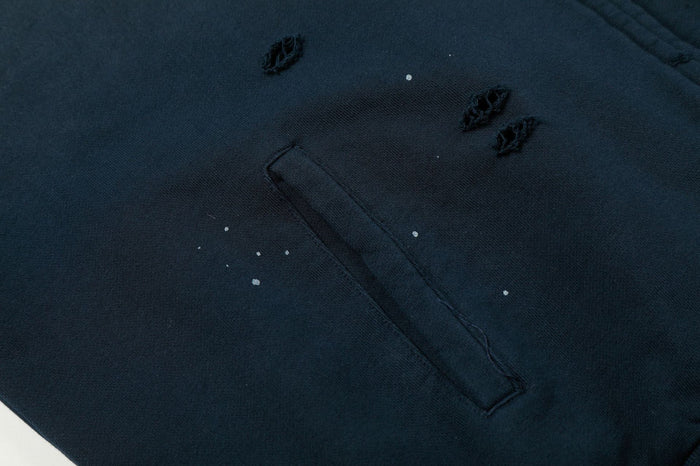 Close-up of a navy hoodie pocket with distressed tears, loose threads and scattered light marks