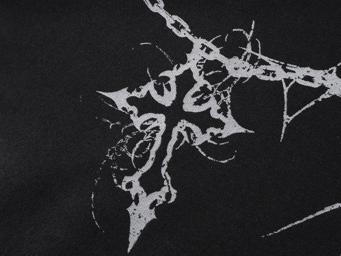 Close-up of white gothic cross and thorn artwork intersected by a chain on black hoodie fabric
