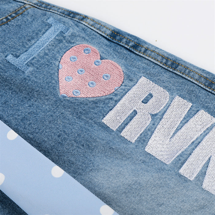 Close-up of light wash denim shorts side print showing a pink polka dot heart and white lettering