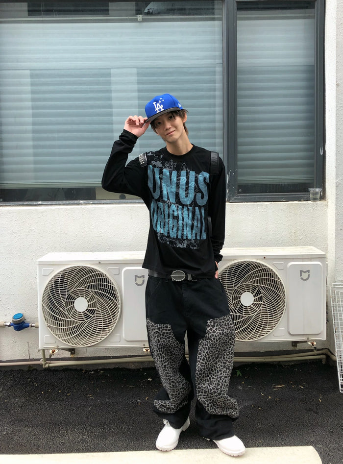 Model adjusting a blue cap while wearing a black long sleeve shirt with a large blue cat graphic