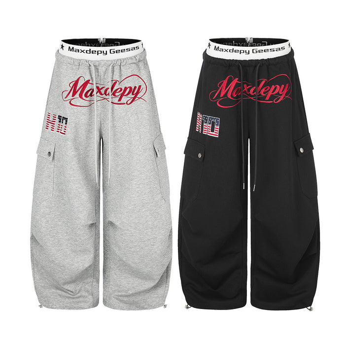 Front view of wide-leg cargo sweatpants in gray and black with red script graphics and side pockets