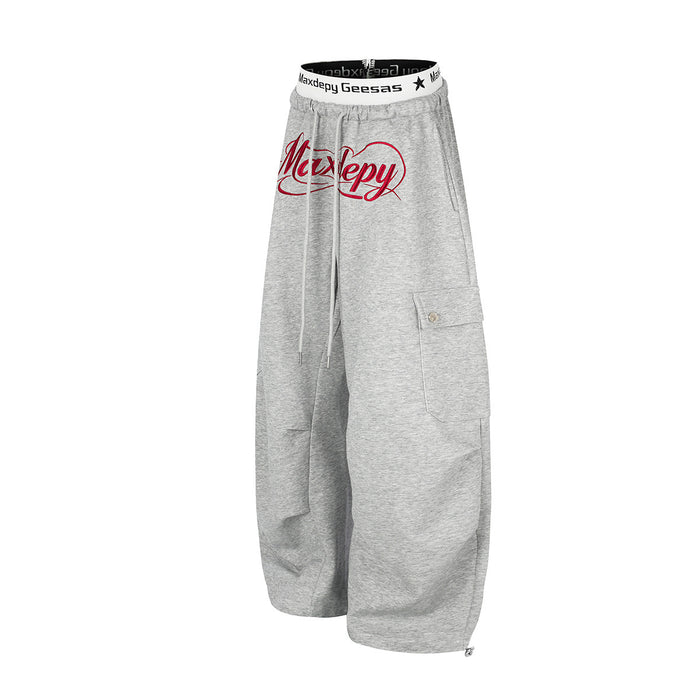 Angled front view of gray wide-leg cargo sweatpants with red script graphic and drawstring waist