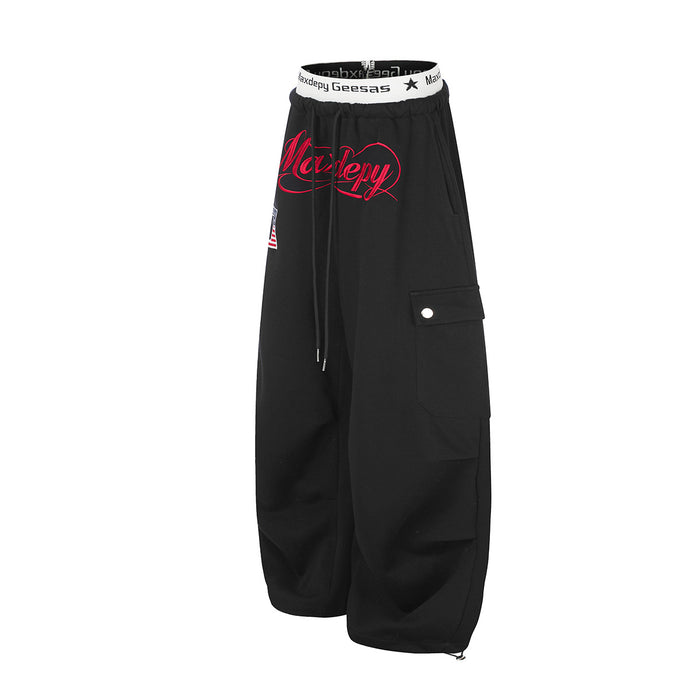Angled side view of black cargo sweatpants showing wide legs, layered side pockets, and red front graphic